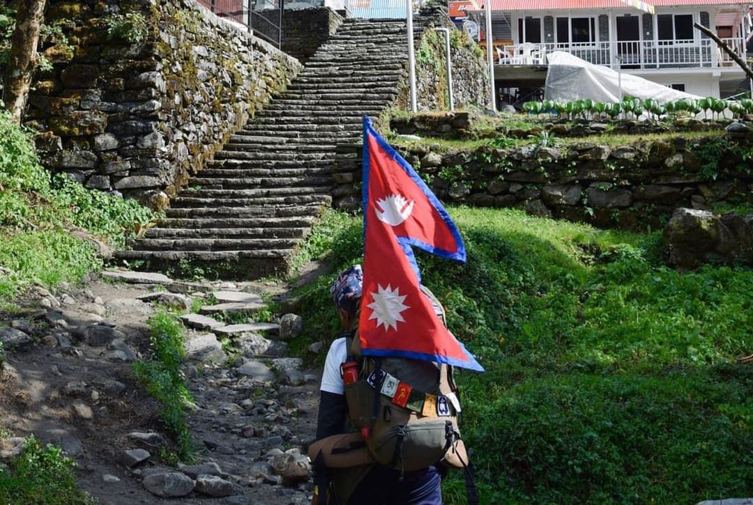 Trekker carrying Nepali flag climbing stone steps toward Chhomrong village on Annapurna Base Camp Trek