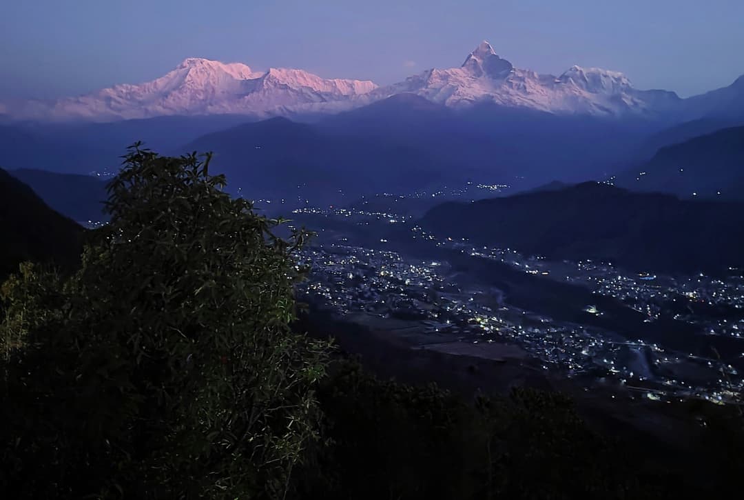 Evening view of illuminated Pokhara city with snow-capped Annapurna and Machhapuchhre peaks glowing pink at sunset