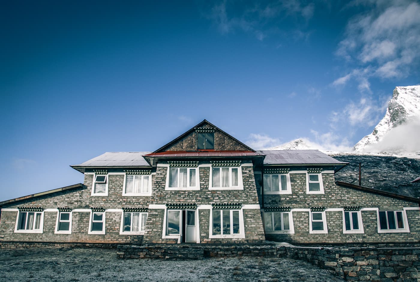 Stone-built Kongde Resort perched on a high ridge with snow-capped Himalayan peaks behind it