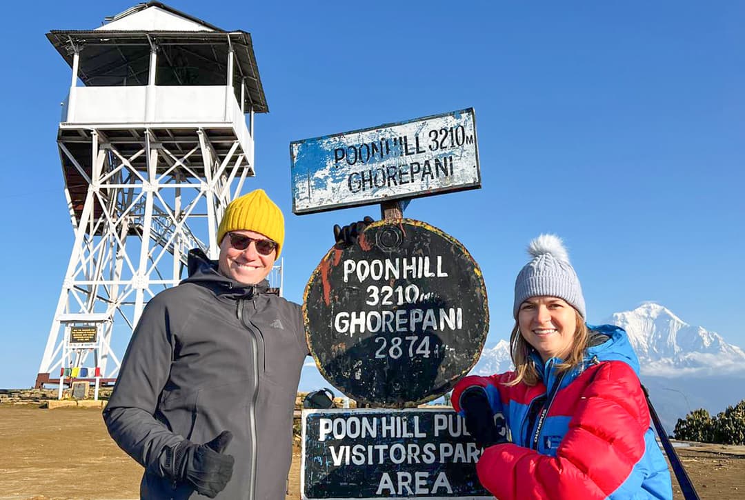 Trekkers Posing Beside The Poon Hill Signpost At 3,210 M With Mountain Views In The Background