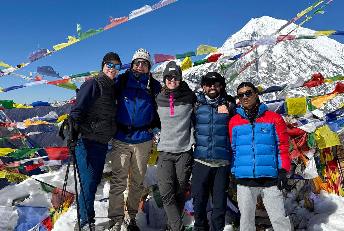 Trekkers posing with prayer flags and snow-covered Langtang mountain views at Kyanjin Ri during the Langtang Valley Trek.